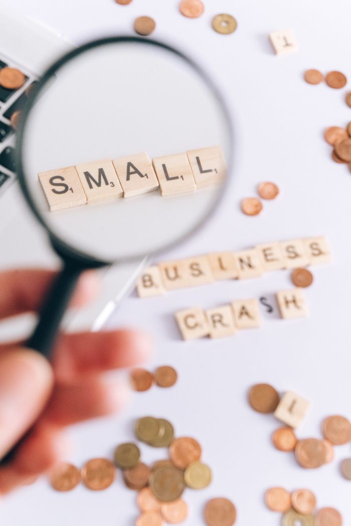 Magnifying glass highlights small business crash concept with coins and letter blocks on white background.